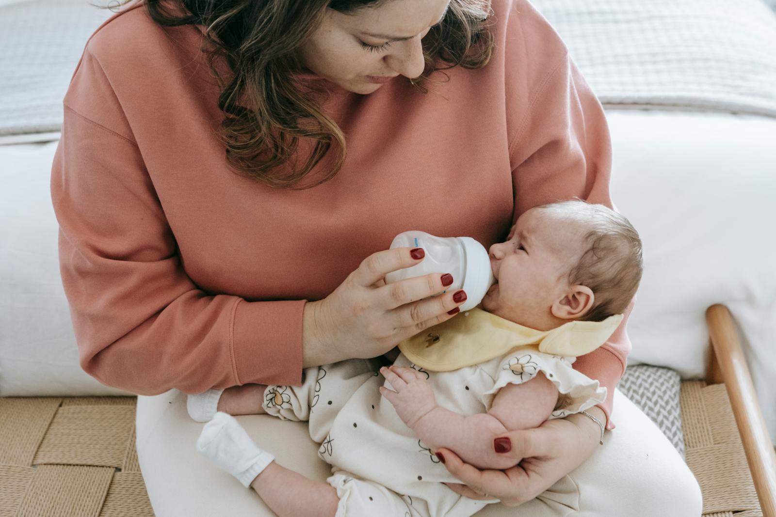 A mother lovingly feeds her baby with a bottle, relaxing in a cozy room setting.