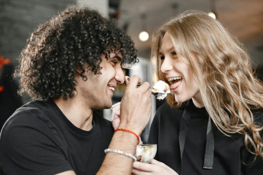 A loving couple shares a joyful moment feeding each other ice cream indoors.