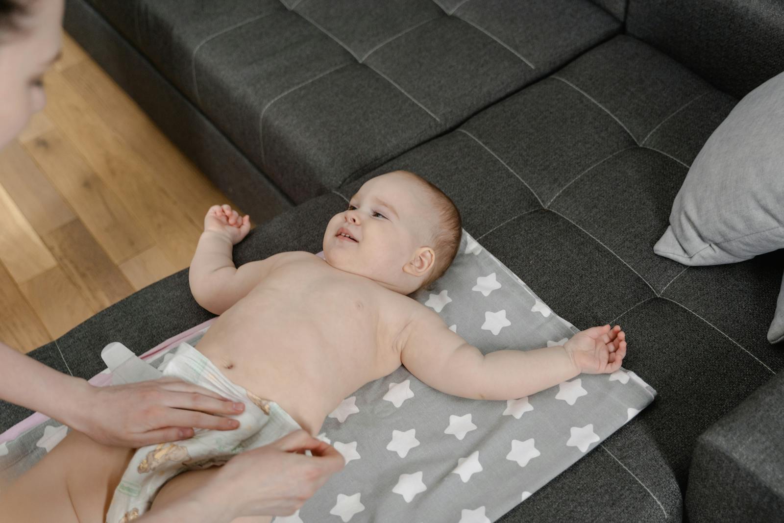 A joyful baby lying on a mat while being changed by a parent in a cozy home setting.