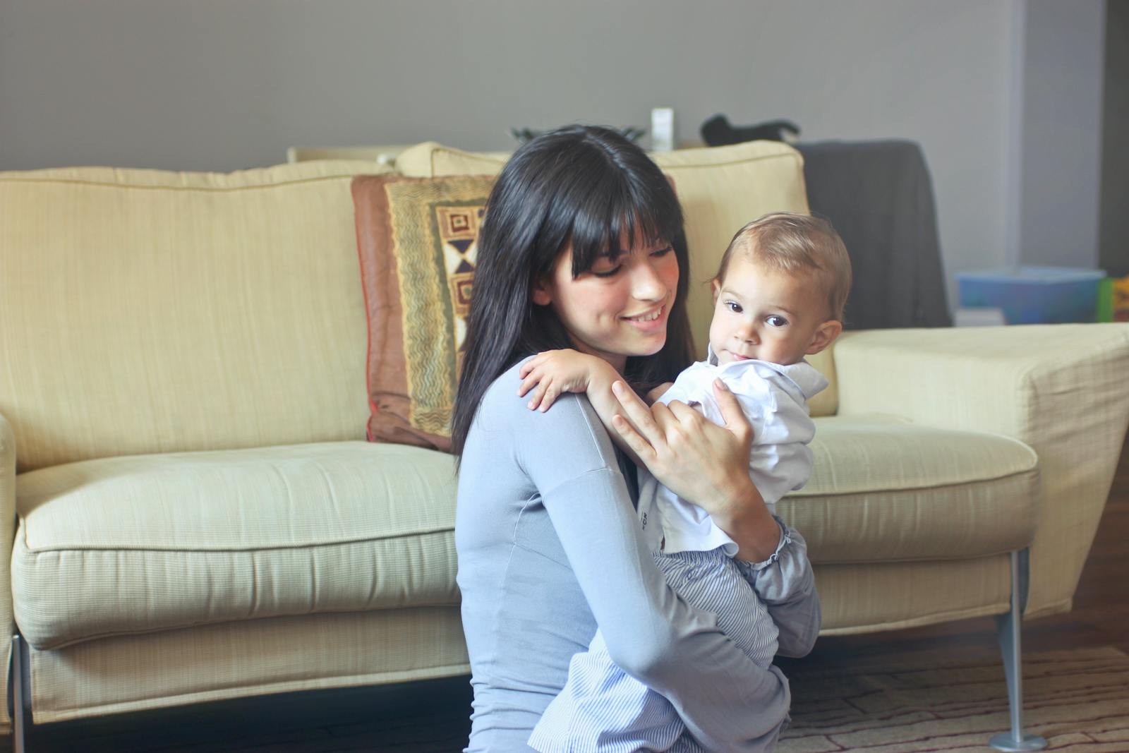 A mother lovingly embraces her baby indoors on a comfortable sofa capturing warmth and togetherness.