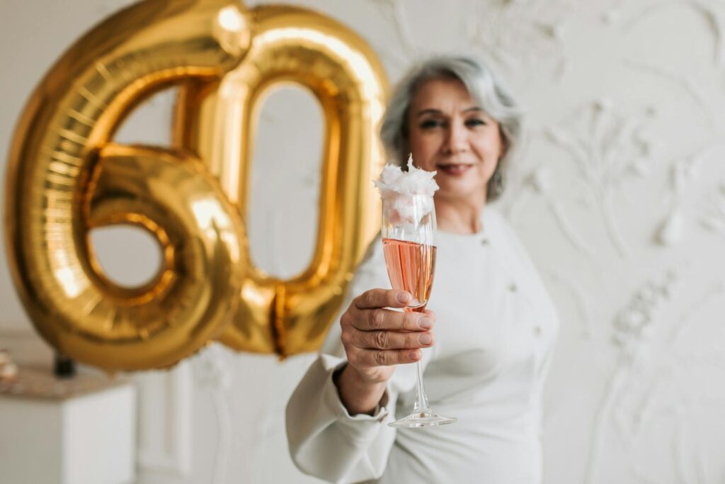 Senior woman celebrating 60th birthday holding champagne in elegant setting.