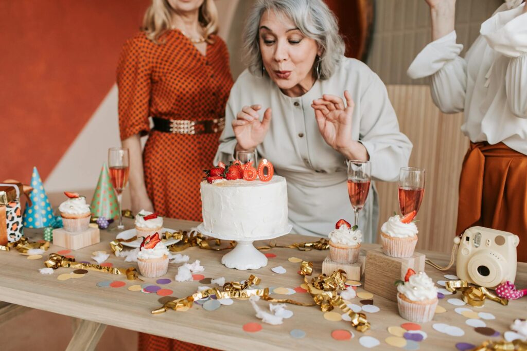 Joyful senior woman blowing out candles on her 60th birthday cake surrounded by friends.