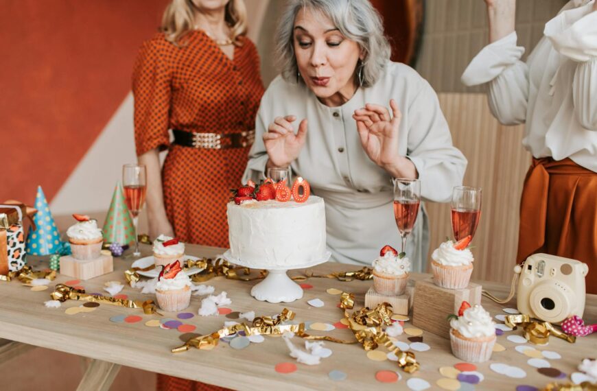 Joyful senior woman blowing out candles on her 60th birthday cake surrounded by friends.