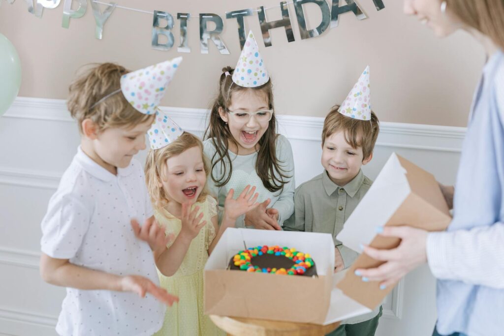 Joyful kids celebrating a birthday with a colorful cake and party hats indoors.