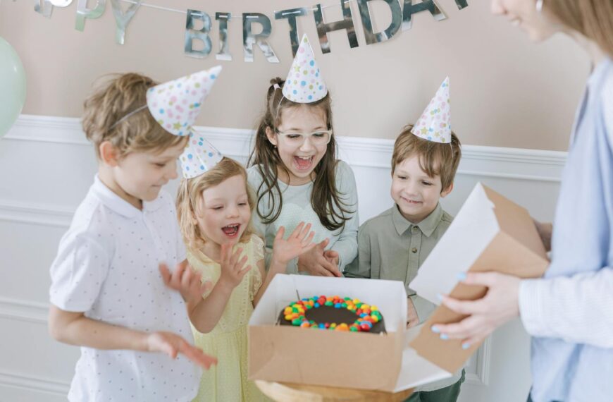 Joyful kids celebrating a birthday with a colorful cake and party hats indoors.