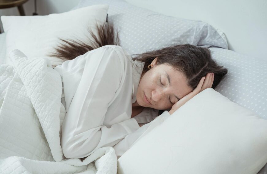 A serene woman rests comfortably in bed with soft pillows and blankets, embracing relaxation.