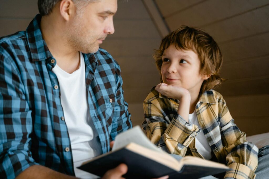 A father and son enjoy a cozy bedtime story together in a warm, indoor setting.