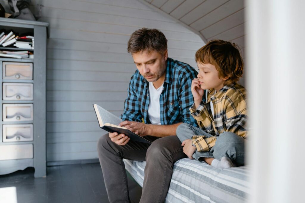 A father and son share a bonding moment while reading together in a cozy bedroom setting.