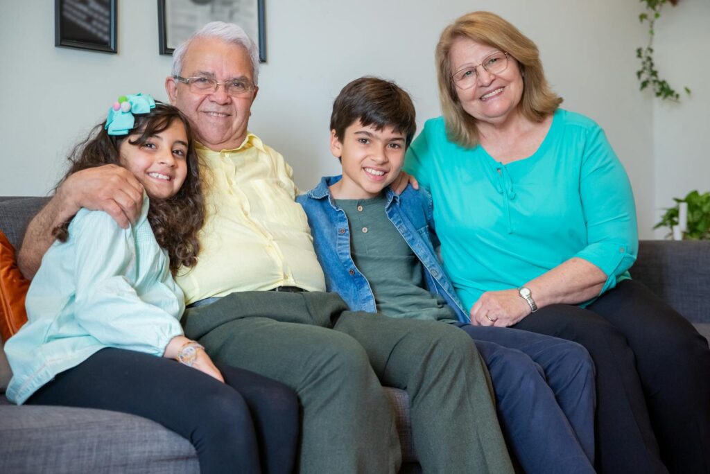 Smiling family with grandparents and grandchildren sitting on a sofa indoors.