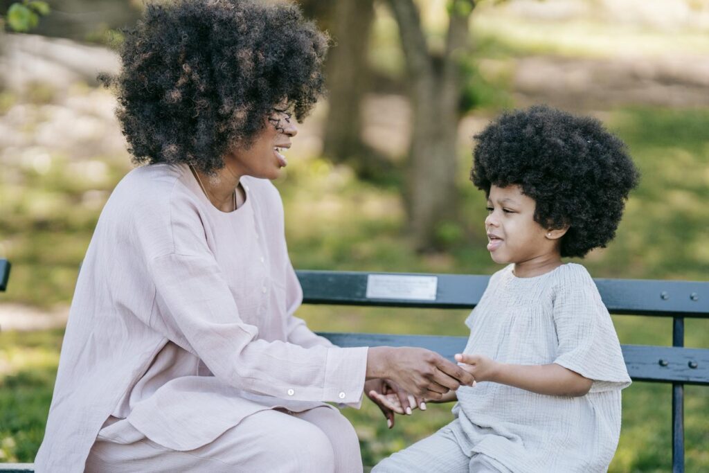 A loving mother and child sitting on a bench, holding hands outdoors.