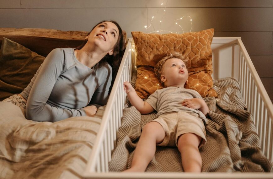 A mother and her toddler relax in a cozy, softly-lit bedroom, creating a warm family moment.