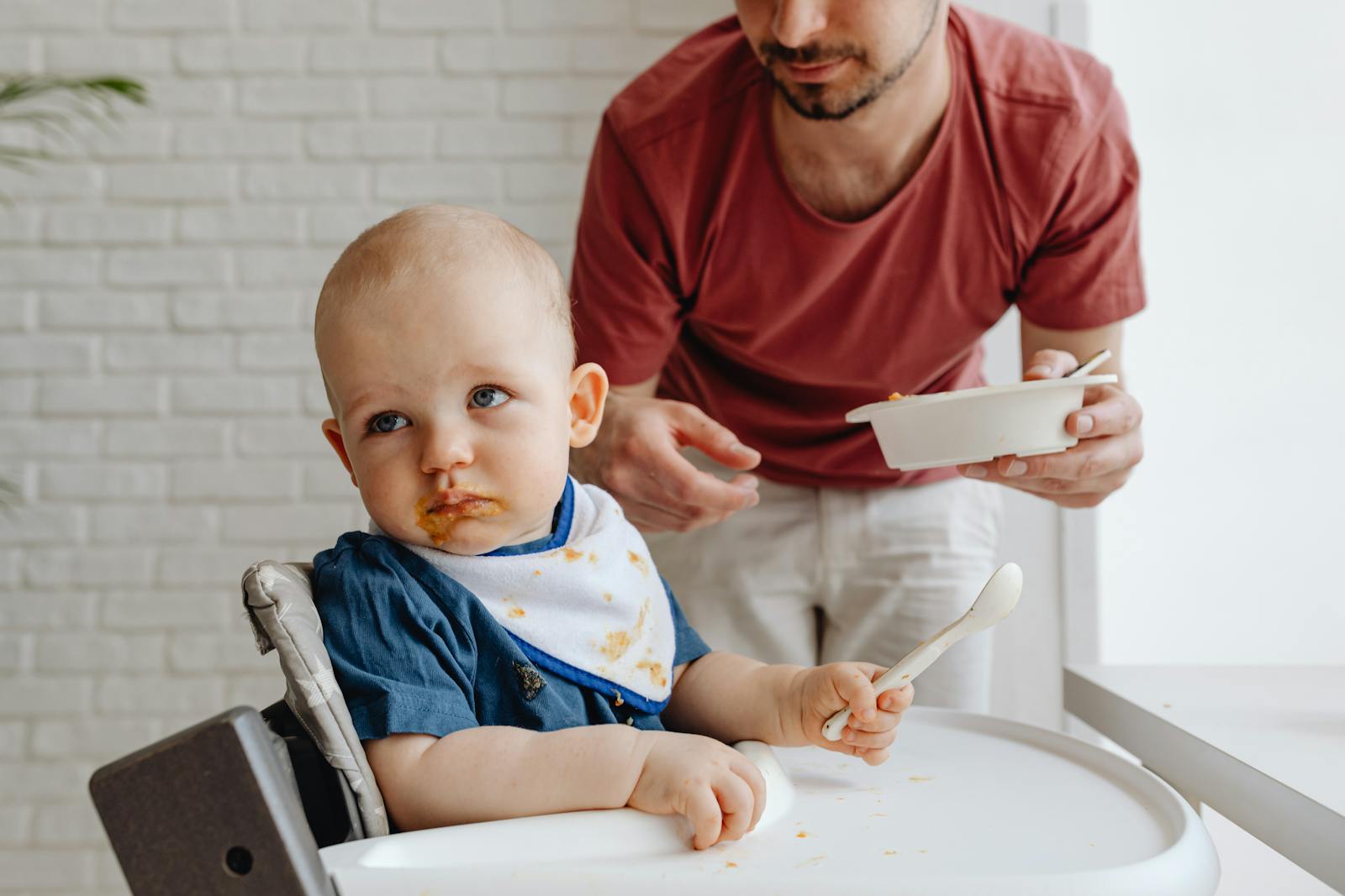 A father feeding his baby in a high chair, showcasing a nurturing family moment.