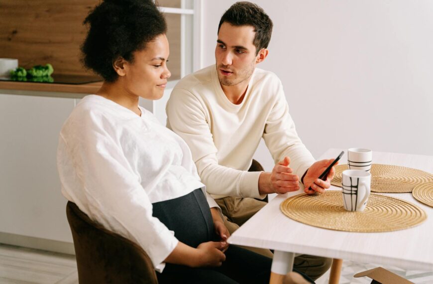 An interracial couple having a discussion about pregnancy while sitting at a kitchen table.