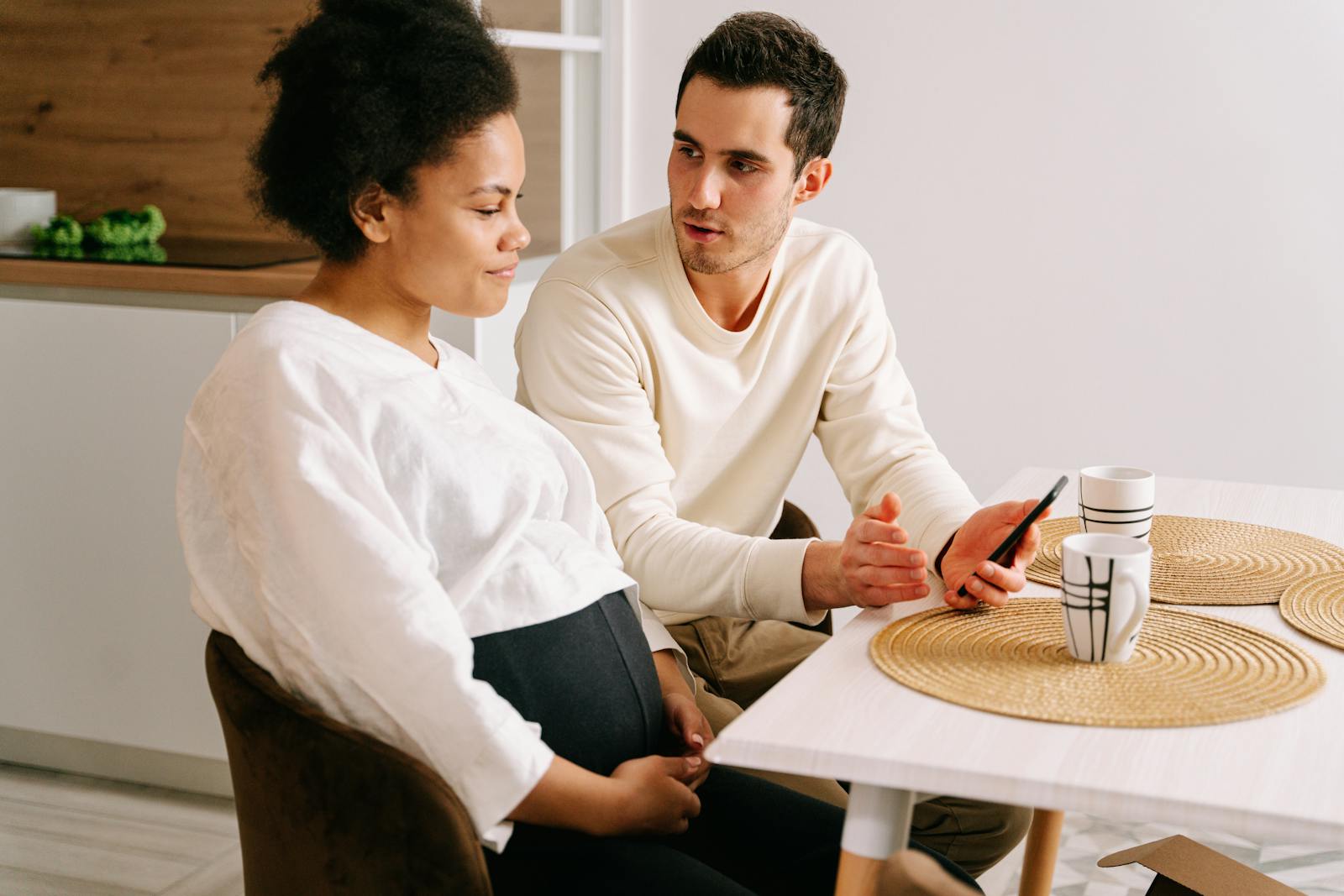 An interracial couple having a discussion about pregnancy while sitting at a kitchen table.