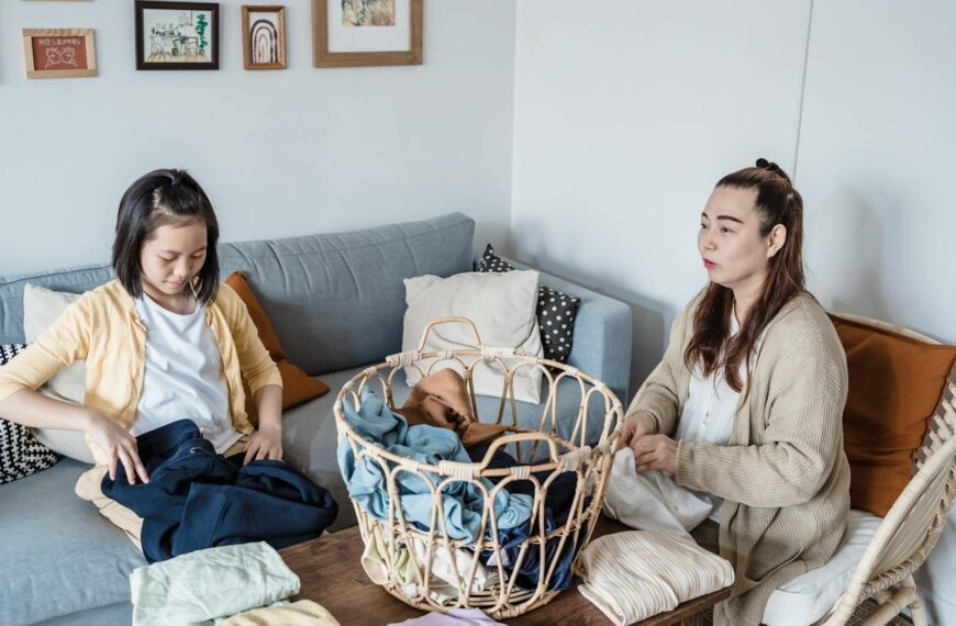 Asian mother and daughter folding laundry on the sofa, engaging in house chores.