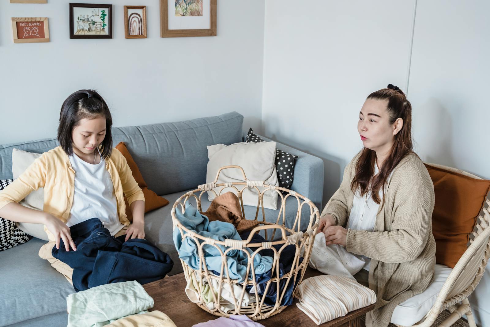 Asian mother and daughter folding laundry on the sofa, engaging in house chores.