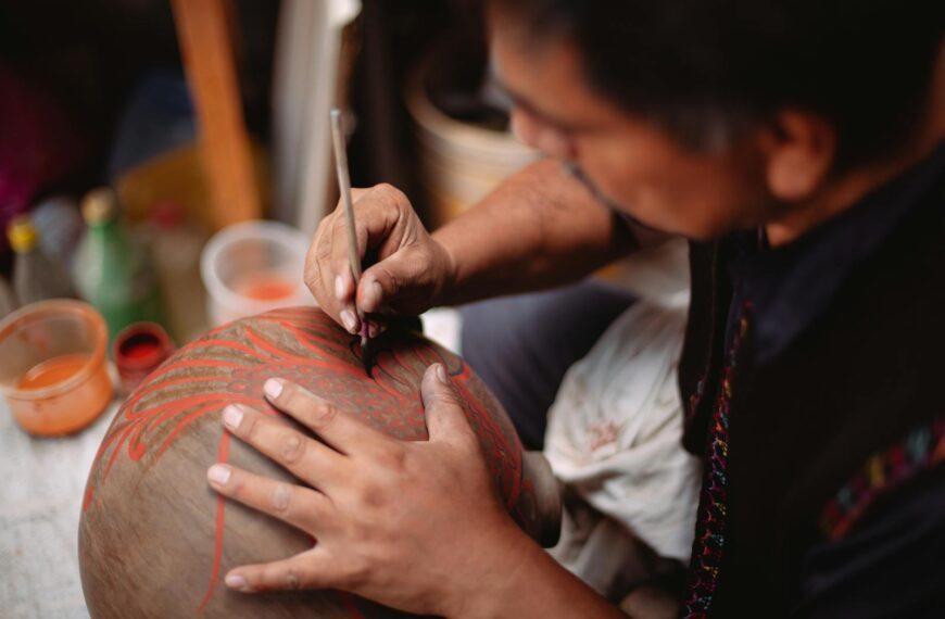A focused artisan carefully painting intricate designs on a clay pot, showcasing craftsmanship.