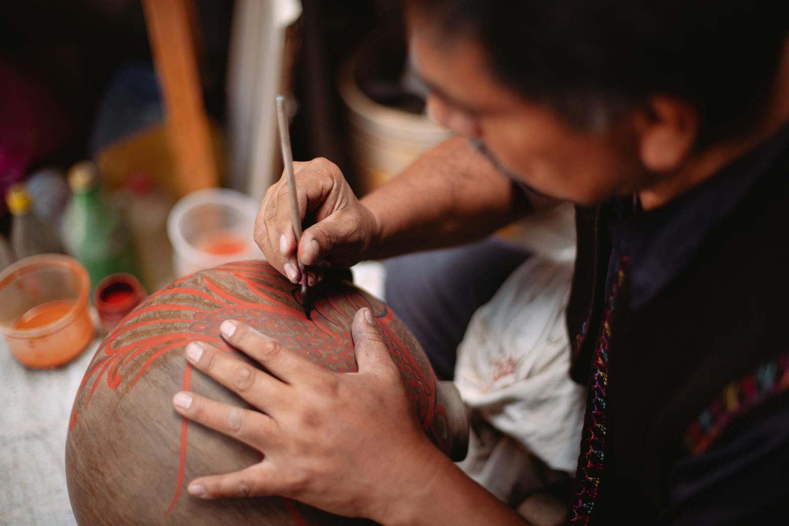 A focused artisan carefully painting intricate designs on a clay pot, showcasing craftsmanship.