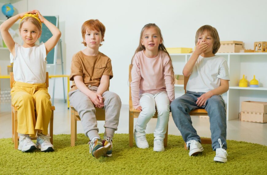Group of children sitting on chairs in a classroom, smiling and engaged.