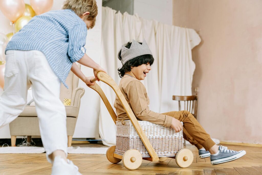 Joyful children playing with a toy wagon indoors, capturing a moment of fun and creativity.