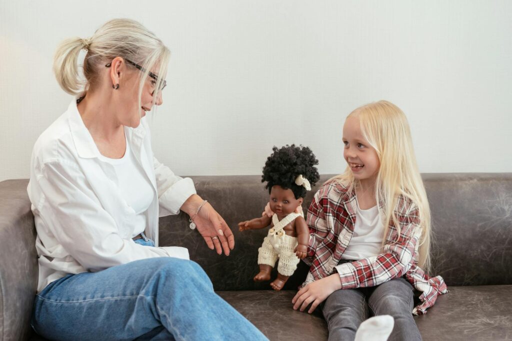 A grandmother and granddaughter enjoy quality time together on a couch with a doll.