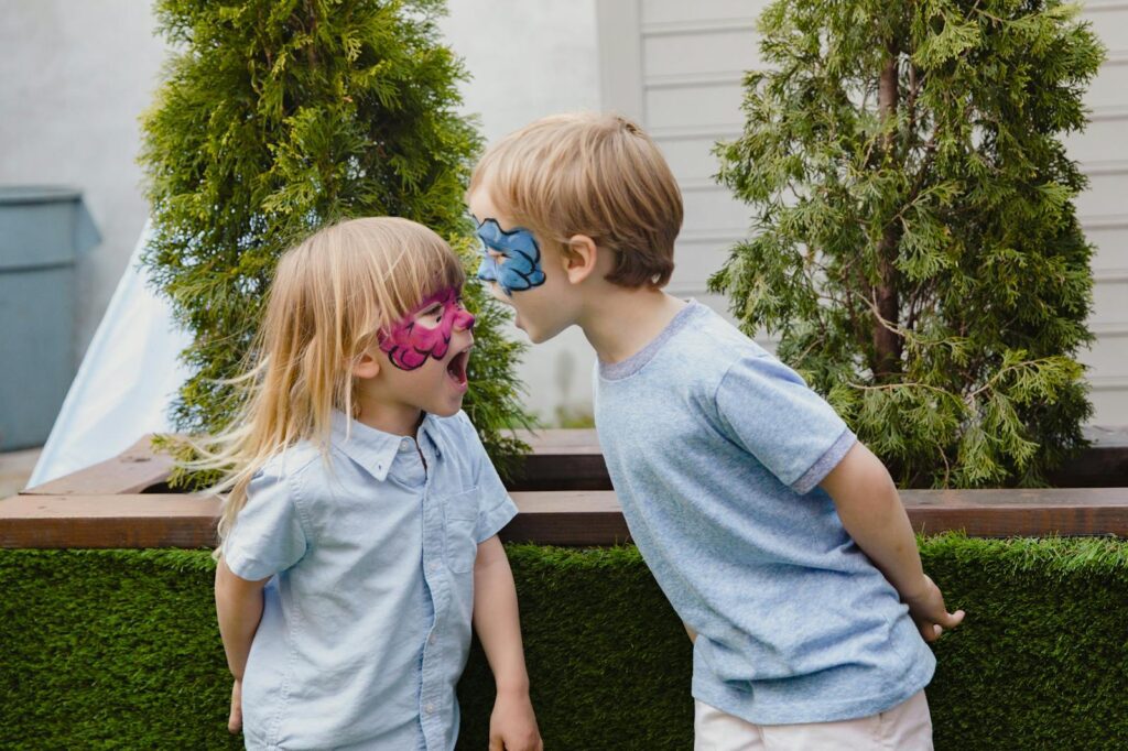 Two children with face paint playfully interacting in an outdoor setting.