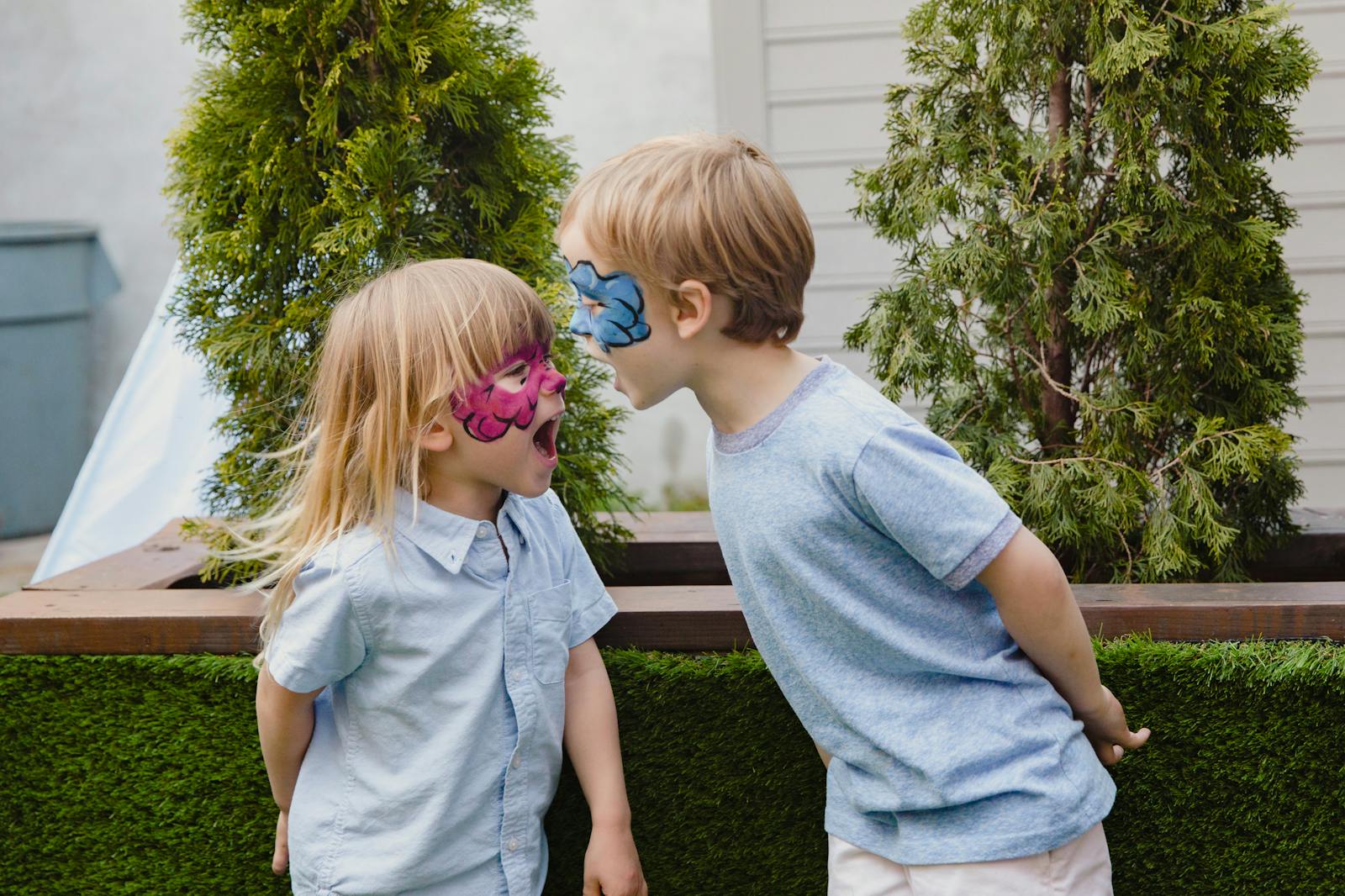 Two children with face paint playfully interacting in an outdoor setting.