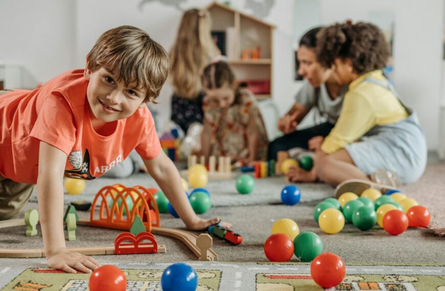 Happy children and a caregiver playing with colorful toys in a lively indoor playroom setting.