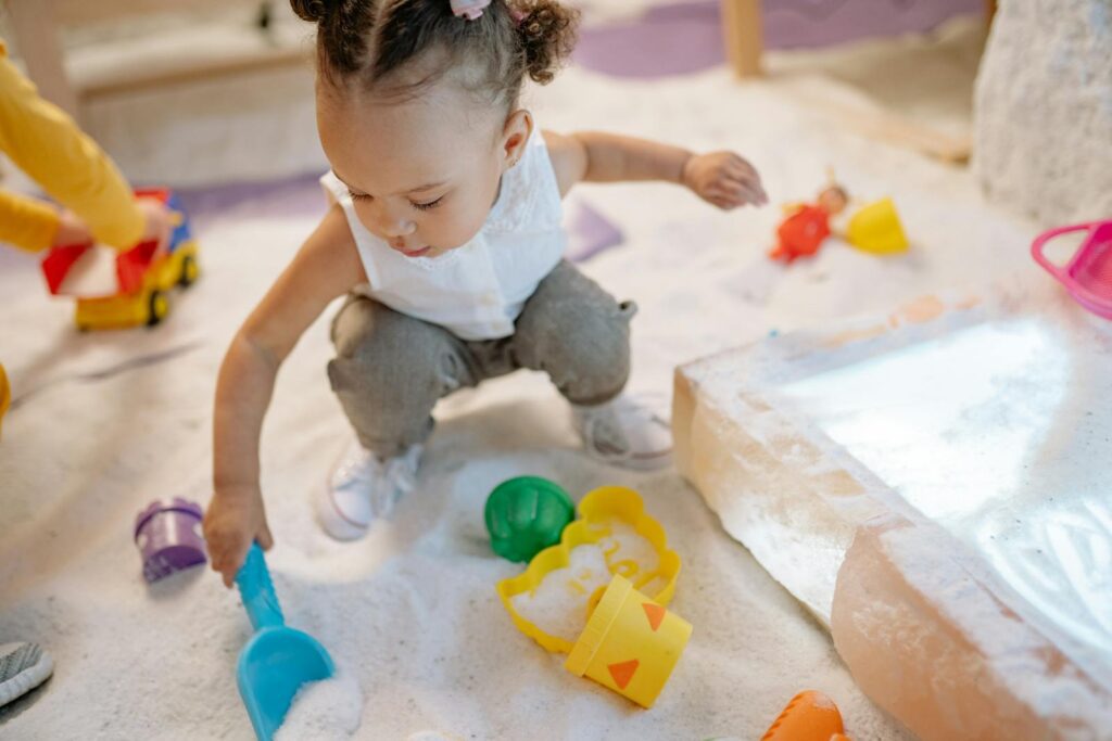 A toddler enjoys playing with colorful sand toys in an indoor play area, exploring and learning.
