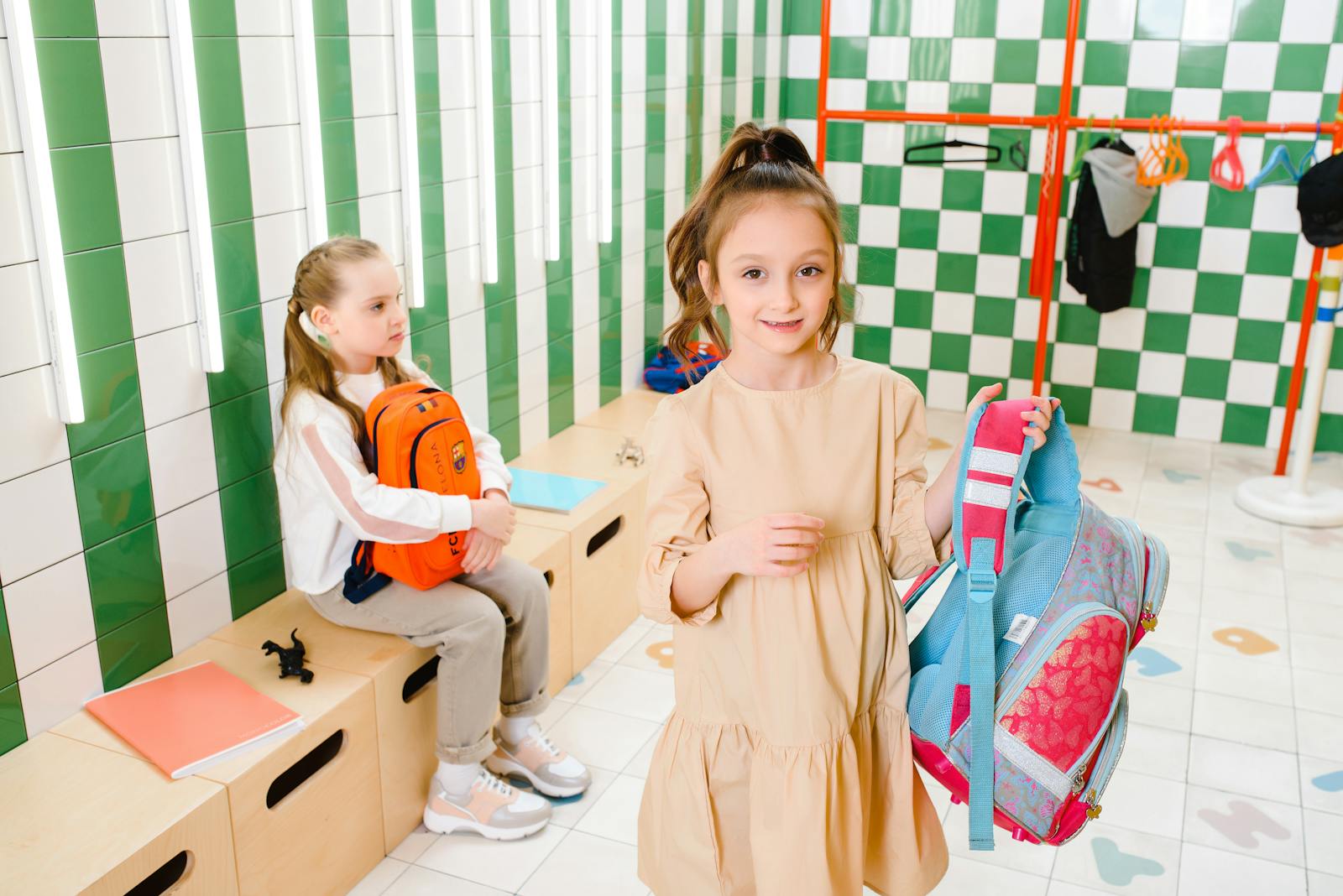Children with backpacks in a vibrant, tiled locker room, smiling and interacting.