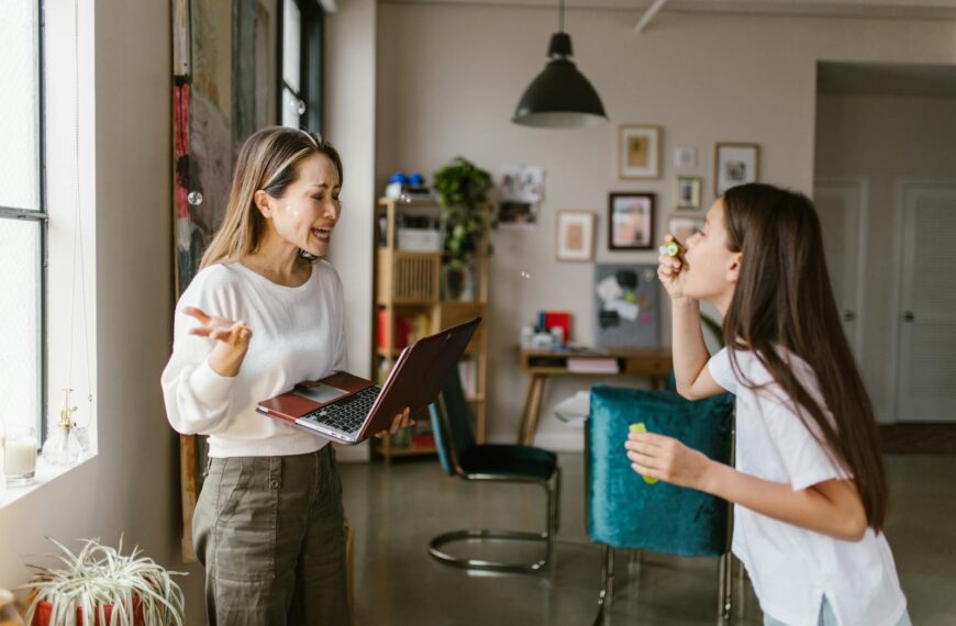 A mother works remotely while her daughter plays with bubbles in a cozy home setting.