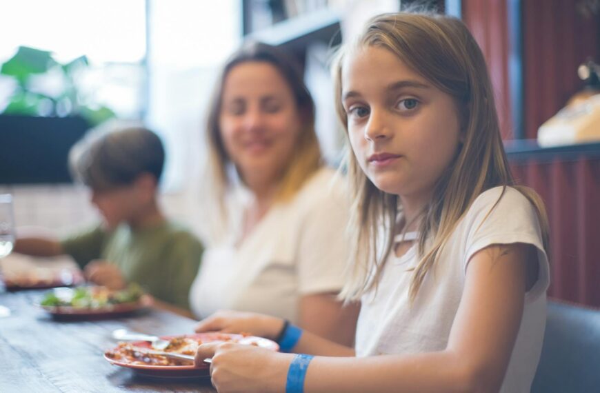 A family enjoying a meal together, focusing on a young girl at the dining table.