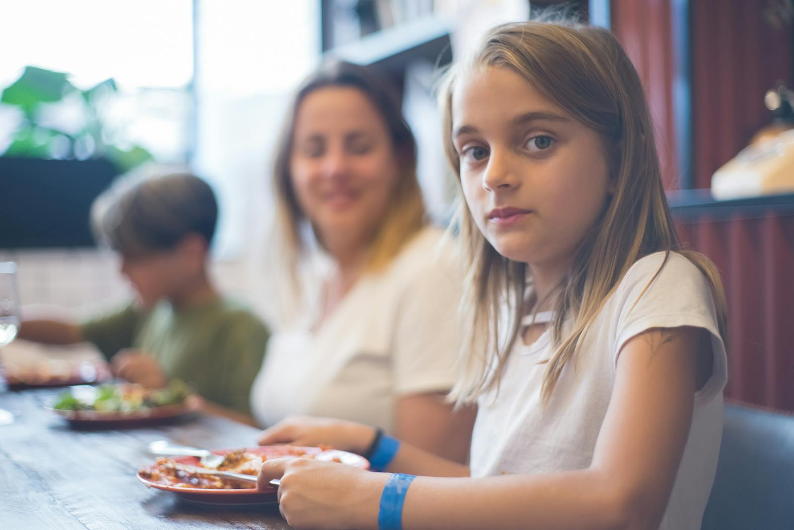 A family enjoying a meal together, focusing on a young girl at the dining table.