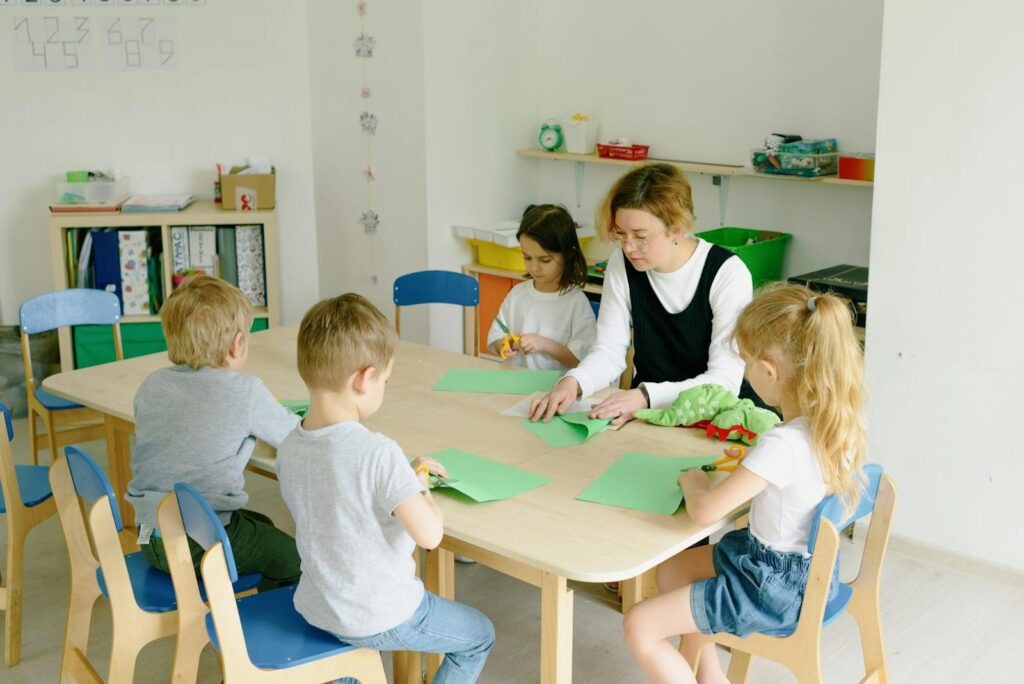Children and teacher engage in a craft session using paper and scissors in a kindergarten classroom.