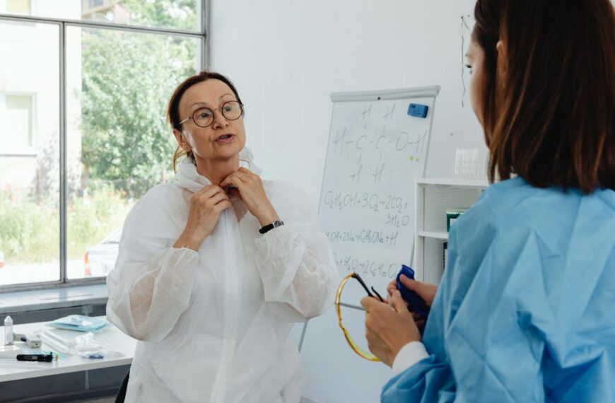 Two healthcare professionals in PPE discussing information in a bright lab.