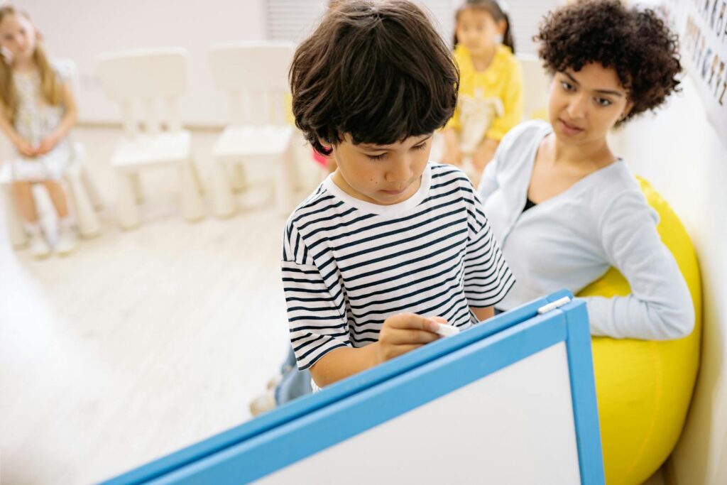 Children interacting with teacher during a classroom activity on a whiteboard, fostering education.