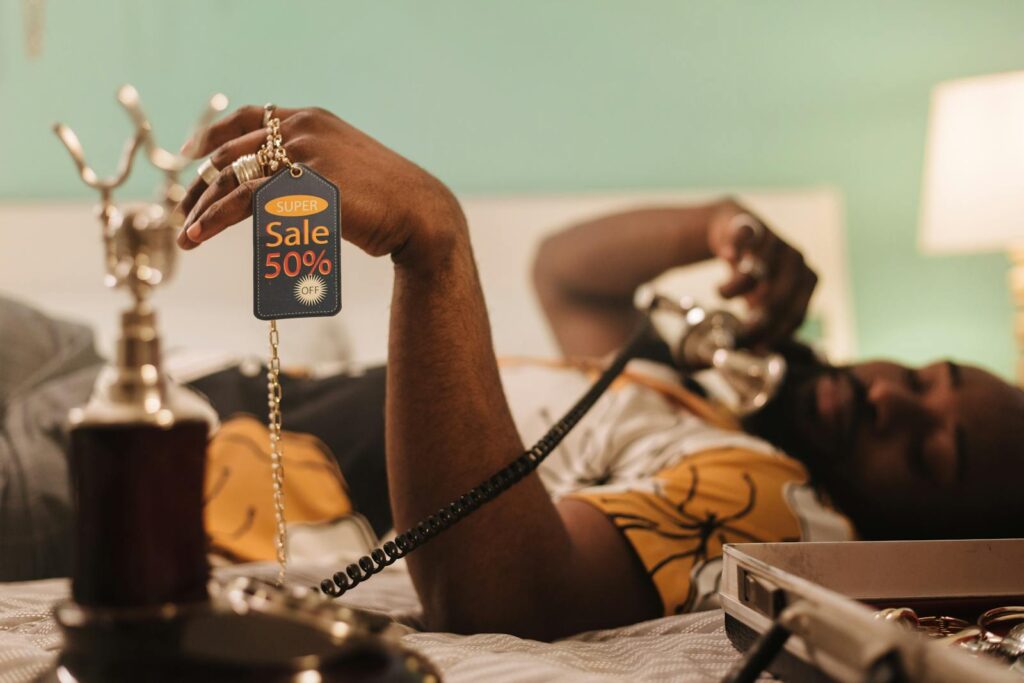 African American man holding a 50% sale tag while talking on the phone.