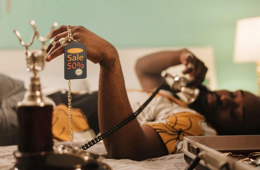 African American man holding a 50% sale tag while talking on the phone.