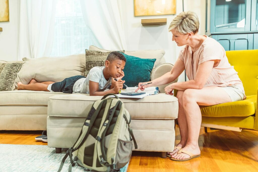 A mother attentively helps her son with his homework in a bright, comfortable living room.