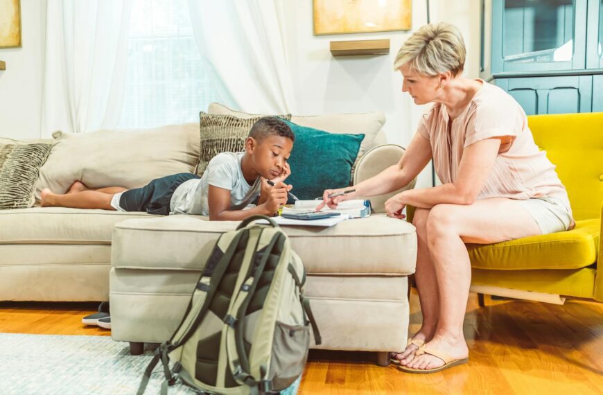 A mother attentively helps her son with his homework in a bright, comfortable living room.