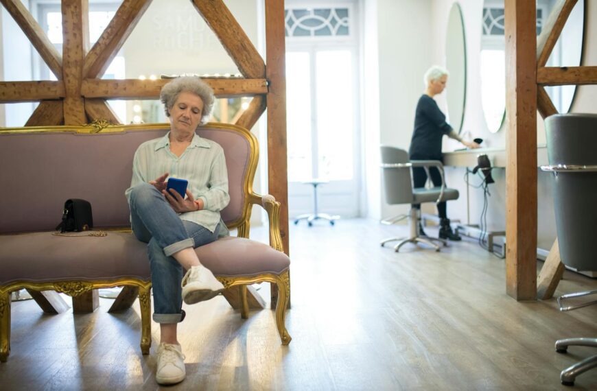 Senior woman sitting on an elegant couch, using her smartphone in a stylish hair salon.