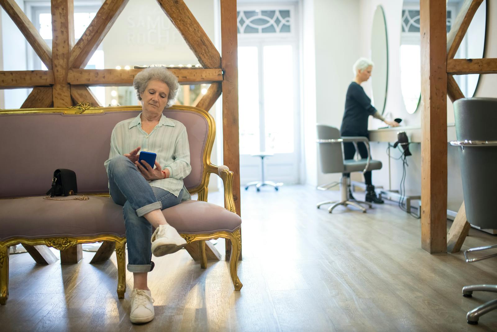 Senior woman sitting on an elegant couch, using her smartphone in a stylish hair salon.
