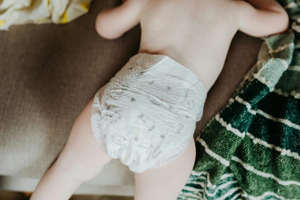 Sweet baby resting on sofa, showcasing soft skin and comfortable diaper, surrounded by cozy blankets.