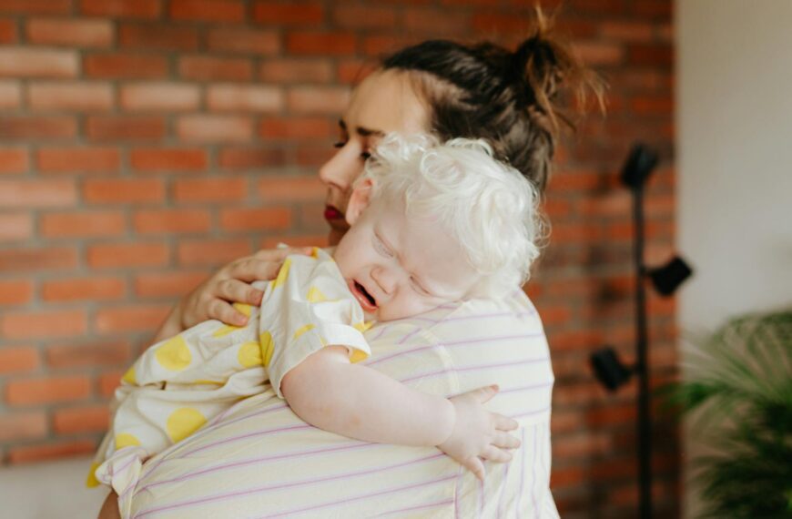 A mother gently holds her crying baby indoors, capturing a tender moment.