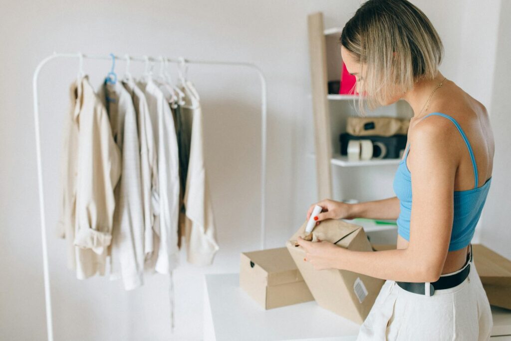 A woman in a blue top packs clothes into a box in a bright room.