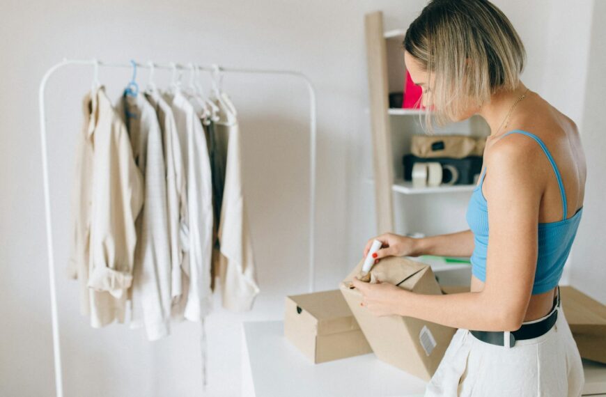 A woman in a blue top packs clothes into a box in a bright room.