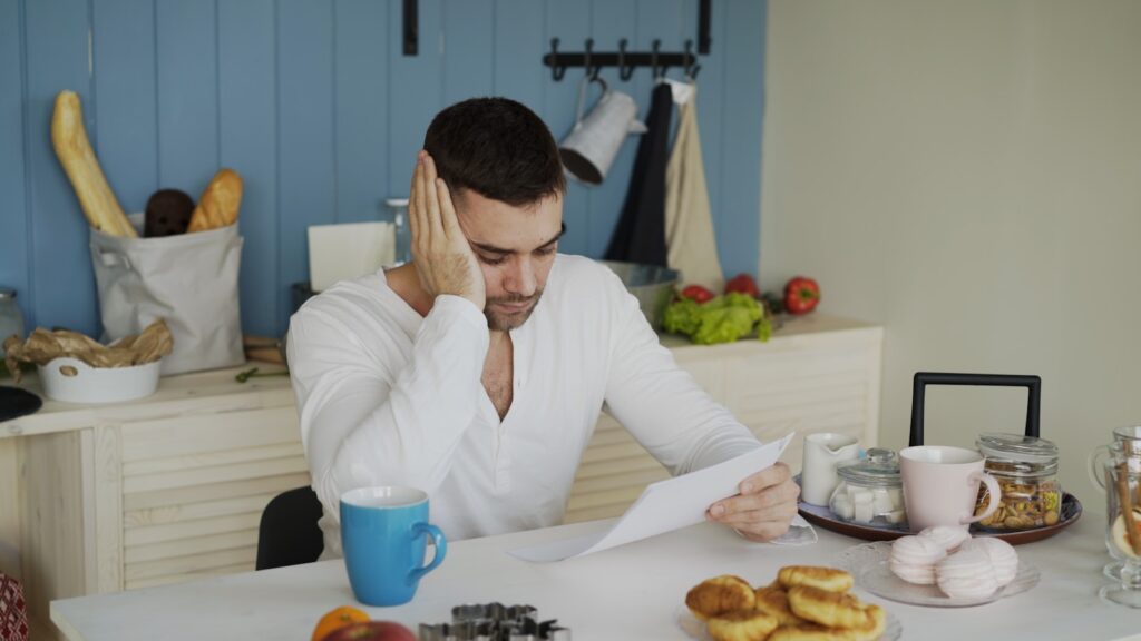 Man sitting at table reading papers with breakfast.
