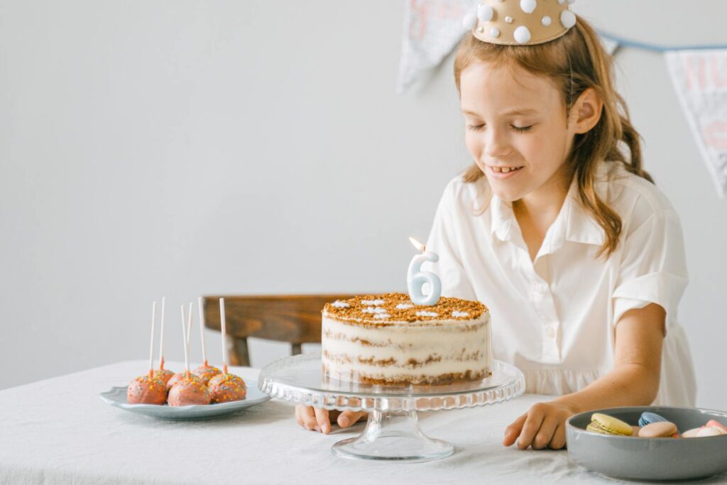 A young girl celebrating her 6th birthday with a cake and a lit candle indoors.