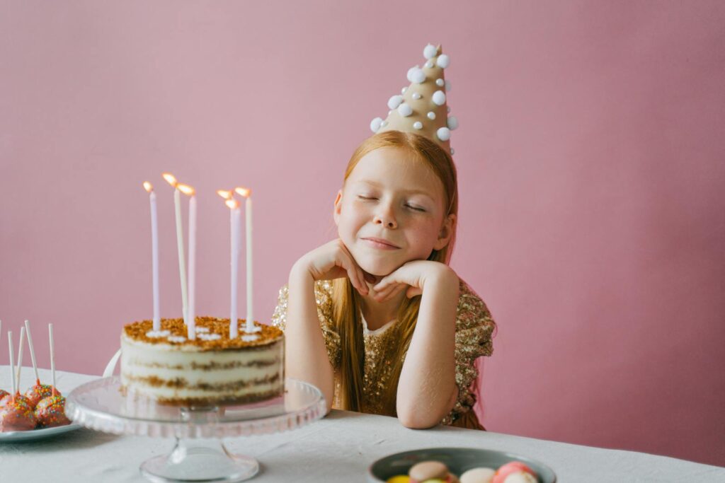 A young girl celebrating her birthday with a cake, wearing a festive party hat.