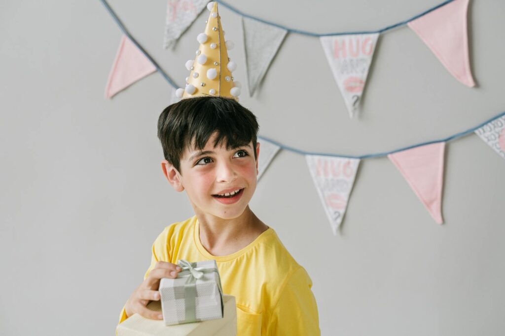 Young boy wearing party hat and holding a gift, celebrating birthday indoors.